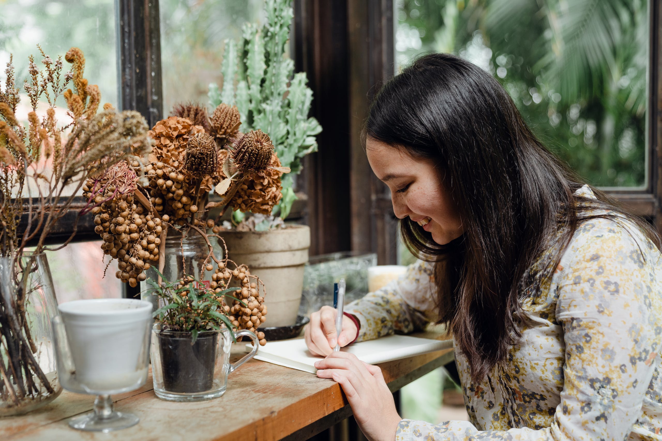 Happy young ethnic woman writing article in cozy workplace