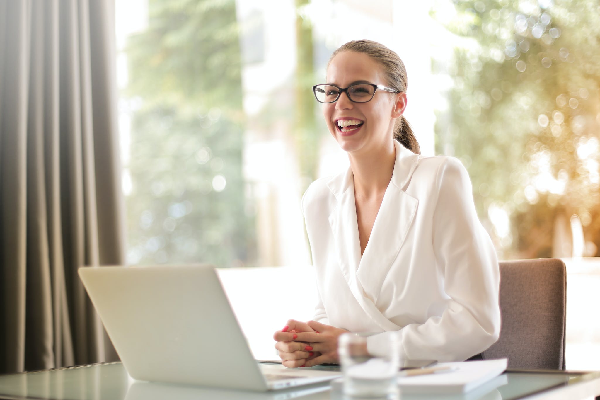 Laughing businesswoman working in office with laptop traits of a successful entrepreneur